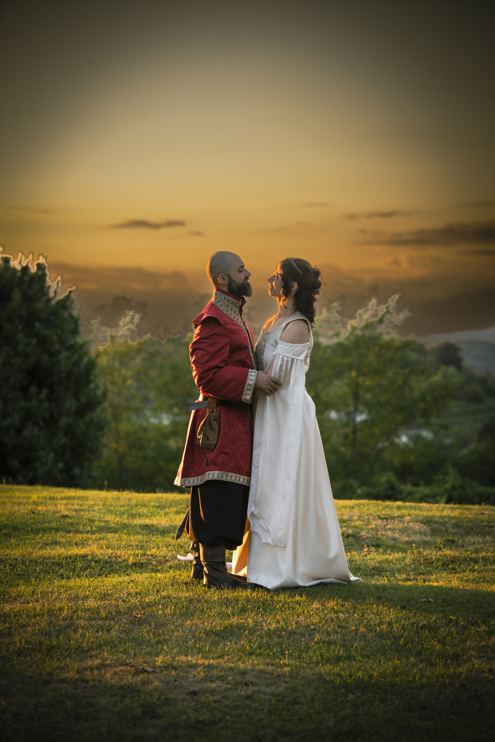 Foto a figura intera di una coppia di sposi vestiti da fiaba mentre si guardano negli occhi al tramonto