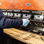 Particolare di una mano di un operaio con un guanto azzurro che lavora su un macchinario industriale