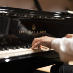 particolare della mano di un pianista mentre suona un piano di marca Steinway & sons