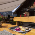 Primo piano di un piatto con salsicce e polenta su un tavolo all'esterno del rifugio alpino Luigi Zacchi, nel comune di Tarvisio