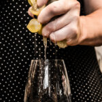 Particolare di due mani femminili che spremono un grappolo d'uva bianca dentro un calice da vino