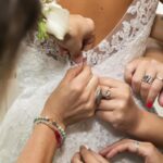 primo piano delle mani delle damigelle che chiudono il vestito della sposa
