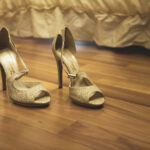 Primo piano della scarpe della sposa davanti al letto au un pavimento di listelle di legno