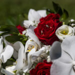 Particolare di un bouquet da sposa composto con rose rosse e bianche. Dentro il bocciolo di una rosa rossa si vedono le fedi degli sposi appoggiate