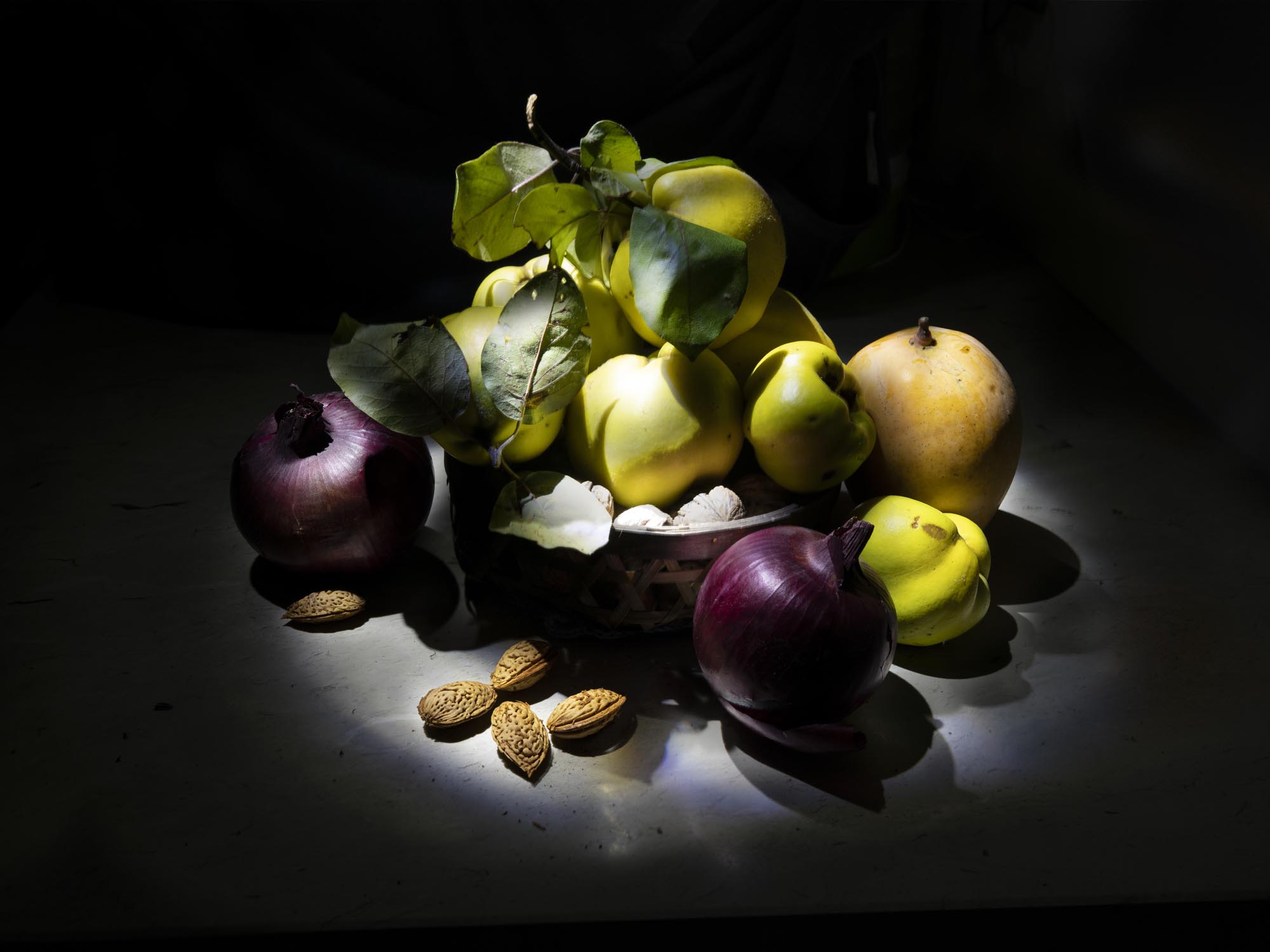 Still life di un cesto di mele cotogne, mango, cipolle di Tropea e mandorle sopra un piano di marmo bianco