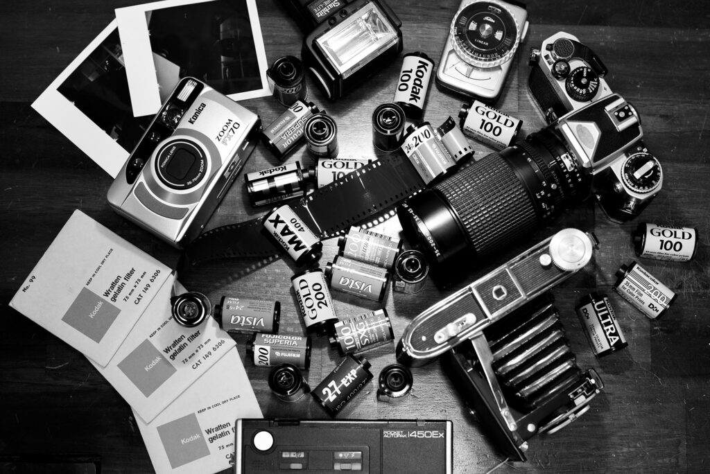 Foto in bianco e nero vista dall'alto di un tavolo di legno sopra cui c'è della vecchia attrezzatura fotografica di vario tipo