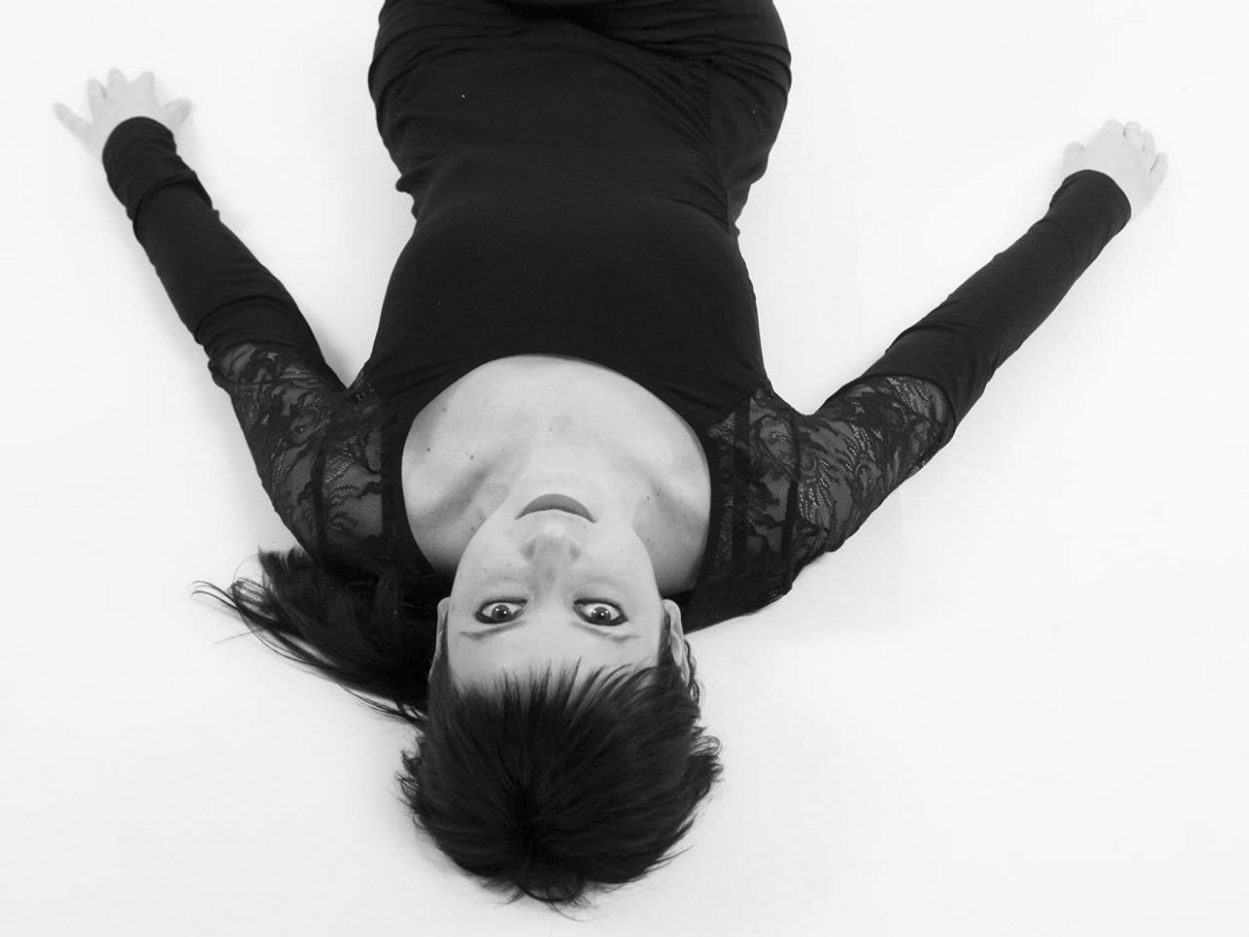 Mezza figura in bianco e nero di una ragazza distesa con un vestito nero e le braccia stese a terra